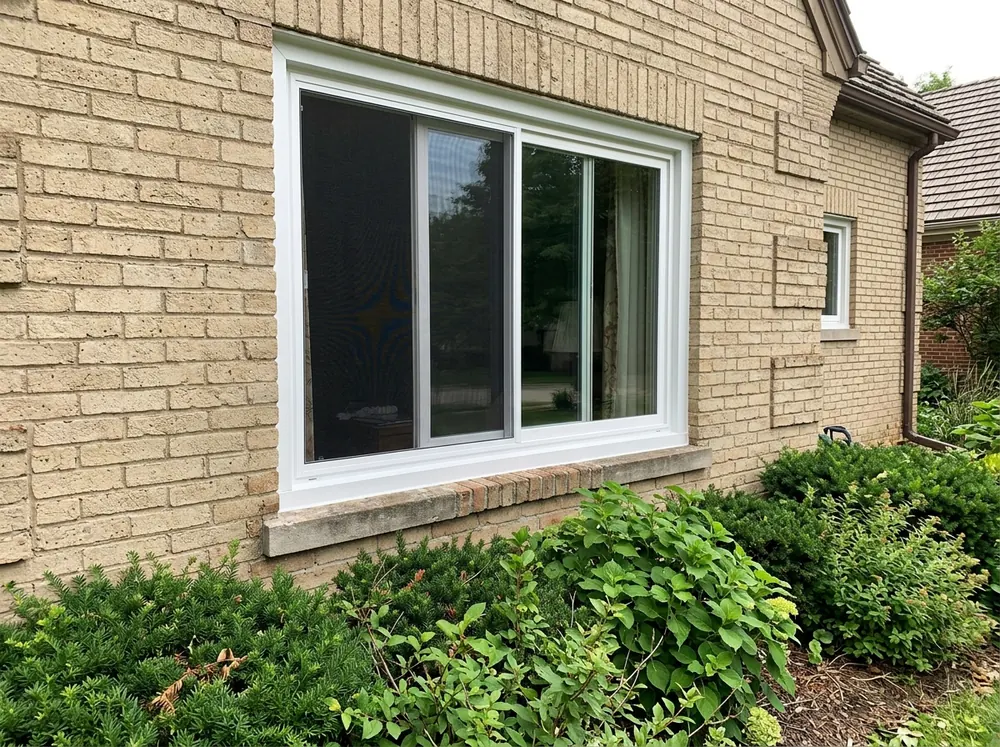 A white two-panel horizontal sliding window with the left sash slid halfway open, on a tan brick wall with a narrow concrete sill